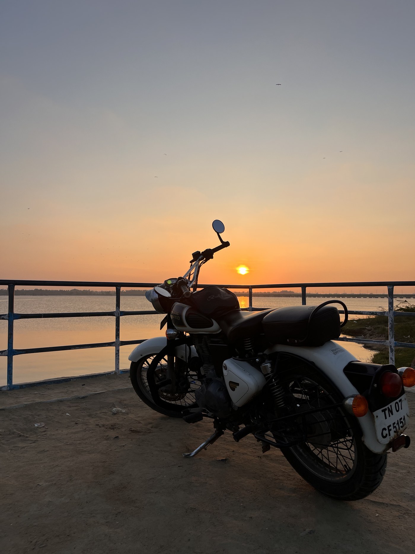 Motorcycle parked by the water at sunset